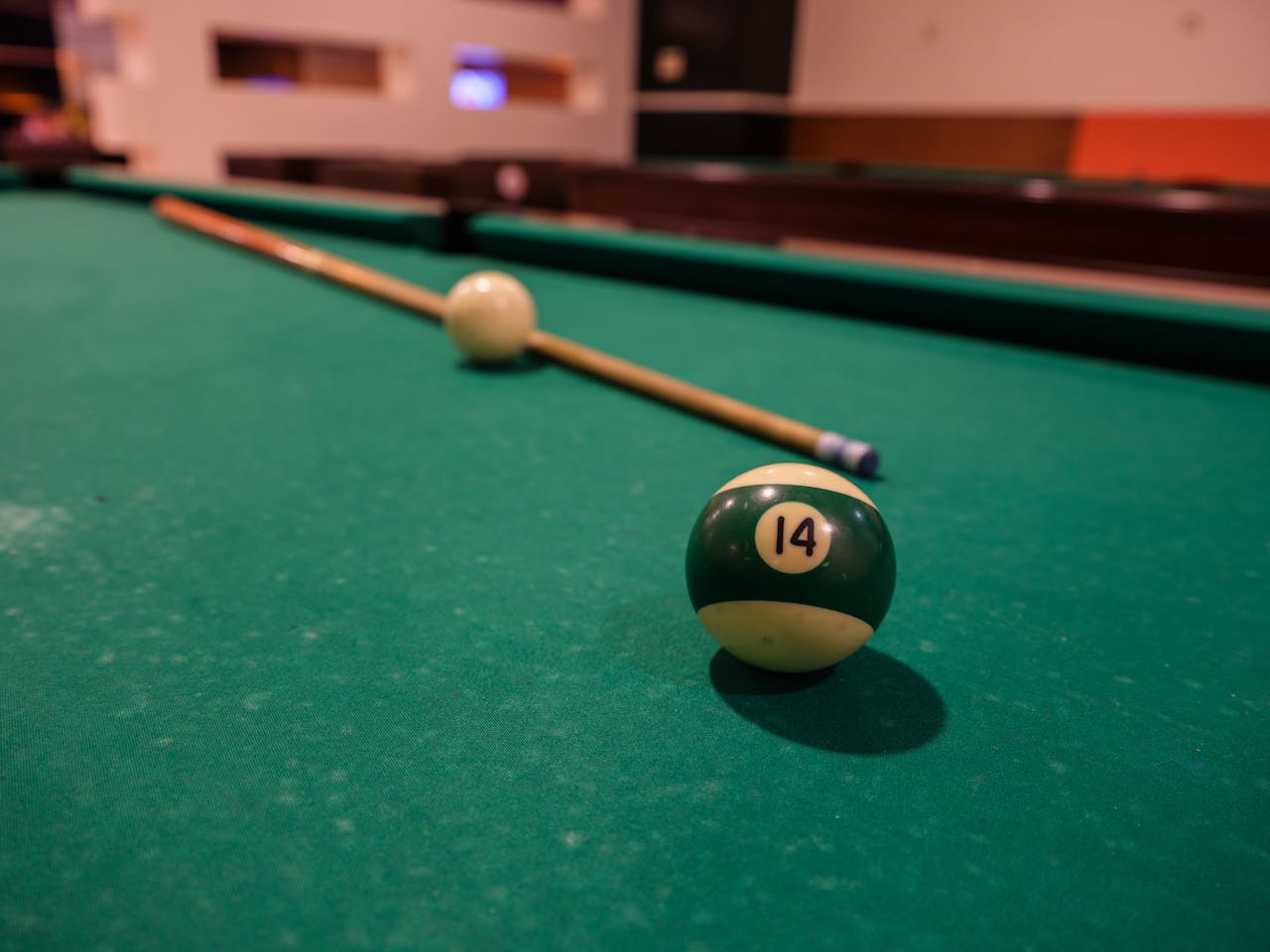 Close-up of a green 14 ball on a pool table with a cue stick in an indoor recreational setting.